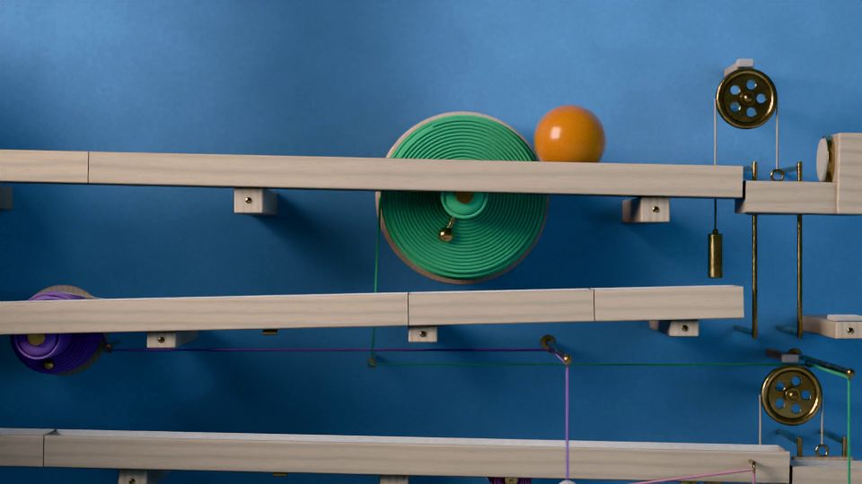 La bola rueda por una balda de haya junto a un carrete de lana verde, delante de una pared azul; a la derecha, una polea de latón con su cuerda.