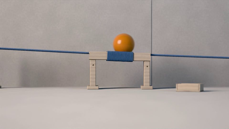 La bola rueda sobre una cuerda tensada entre postes de madera y pasa por un puente con la cuerda enrollada, delante de una pared gris perla.
