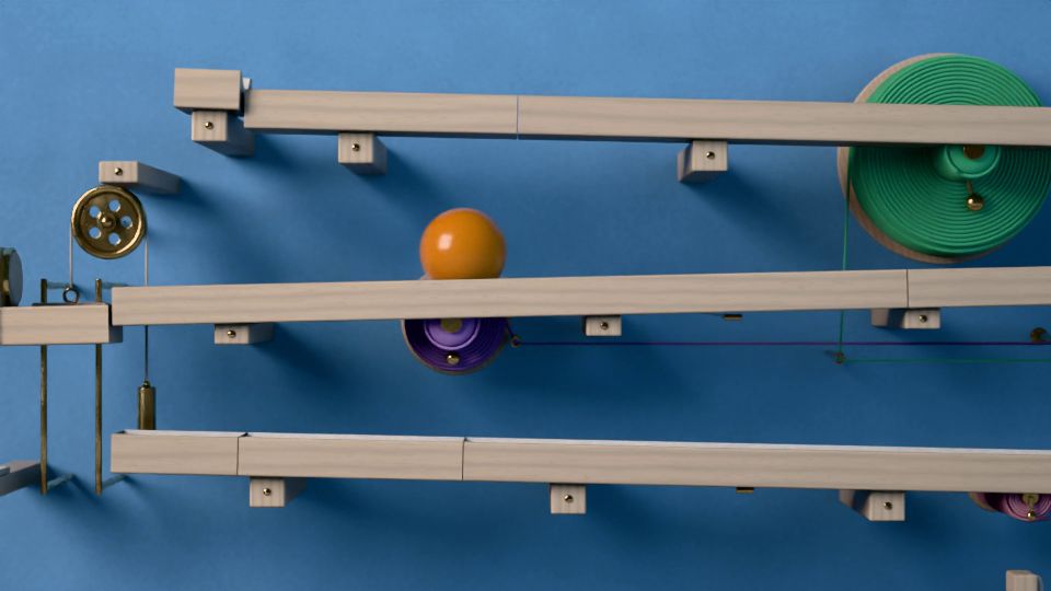 De cerca: la bola rueda por una balda de haya entre una polea de latón con su contrapeso, un carrete de lana lila y otro verde, sobre una pared azul.